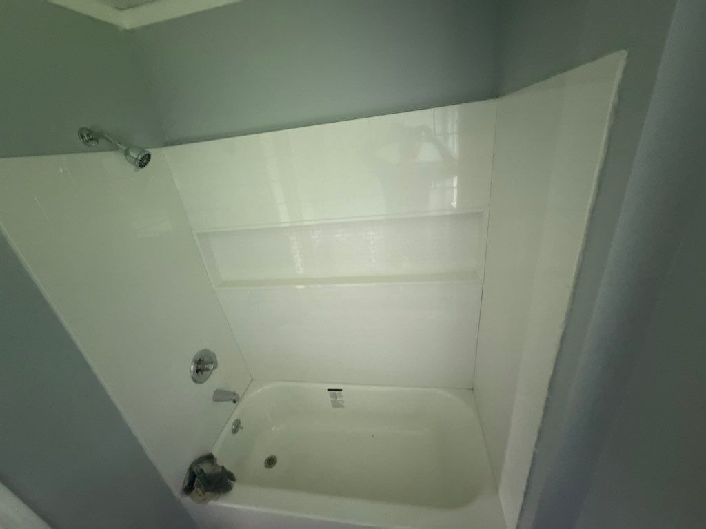 White bathtub and shower surround with built-in shelves in a bathroom with light blue walls.