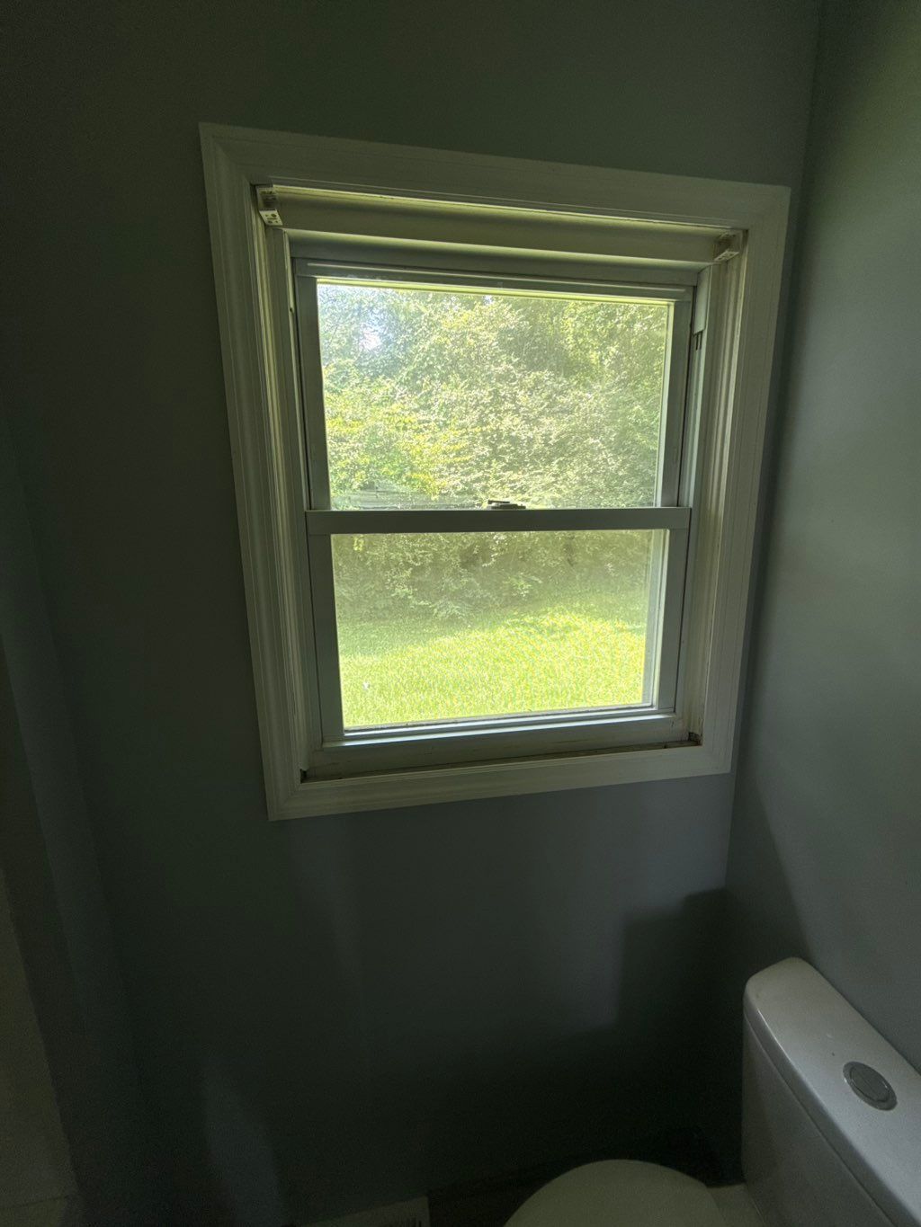 Small, white-framed window in a gray-painted bathroom. Toilet is visible in the bottom right corner.