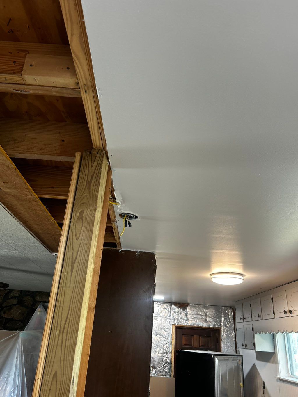 Wooden beam supports an unfinished ceiling with a light fixture. A door and insulation are also visible.