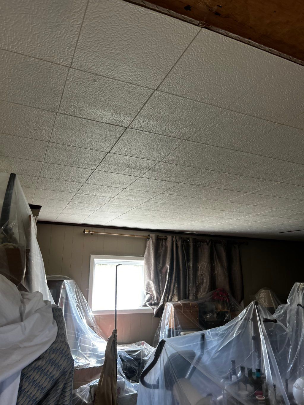 Room interior with textured ceiling, window, and items covered in plastic sheeting.