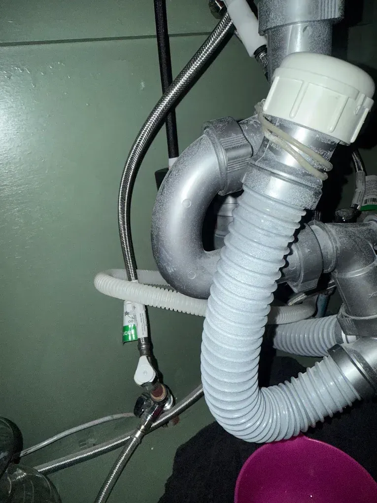 Plumbing under a sink: gray pipes and a flexible hose connecting to a water valve.