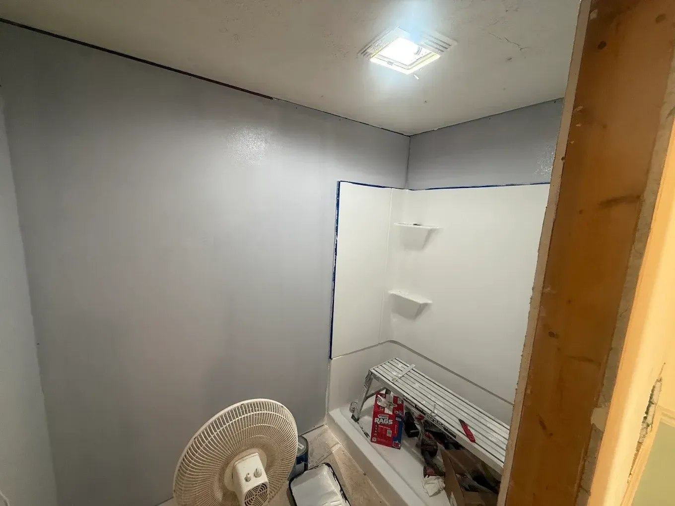 A small, gray-painted bathroom with a white shower stall and an electric fan.