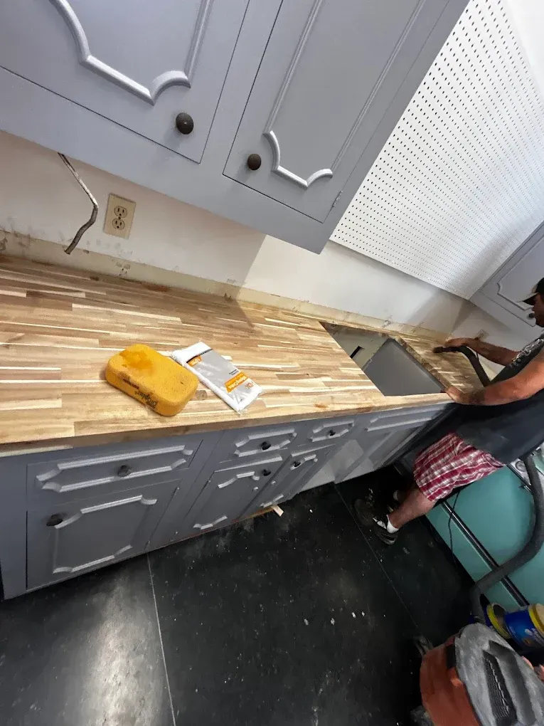 Person installing a butcher block countertop on gray cabinets in a kitchen.