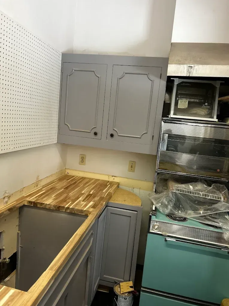 Gray kitchen cabinets with wood countertop, pegboard, appliances, and turquoise refrigerator.