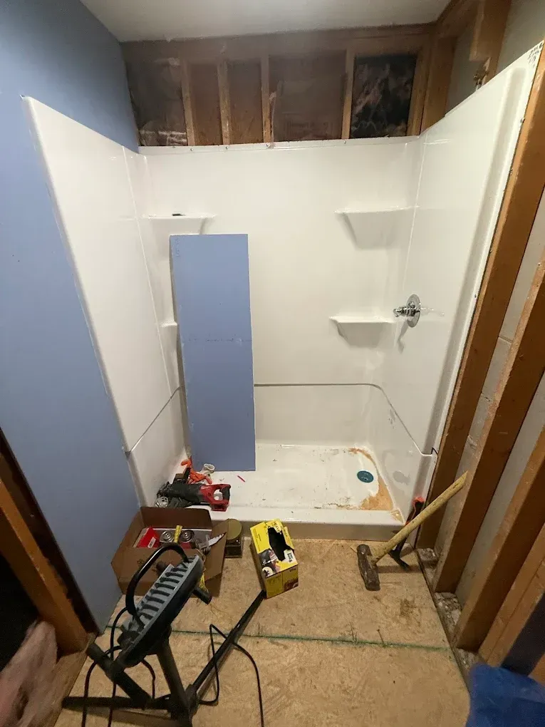 Bathroom renovation in progress, shower stall partially installed, tools on the floor, studs exposed, blue walls.