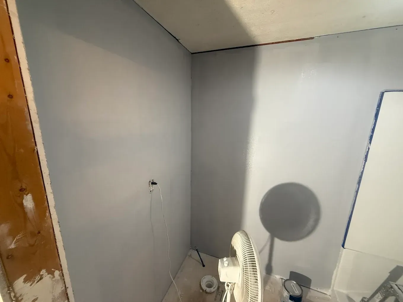 Room with light blue painted walls, fan, electrical outlet, and tape.