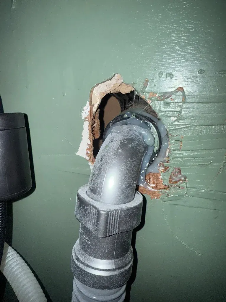 Black pipe elbow exiting a hole in a green wall.