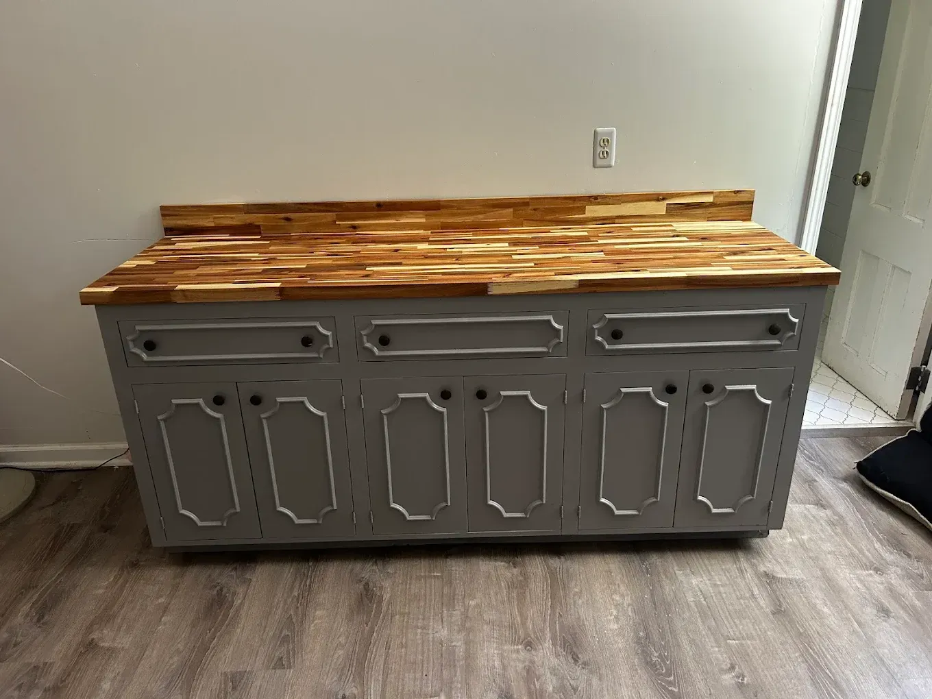 Gray bathroom vanity with wooden countertop against a wall.