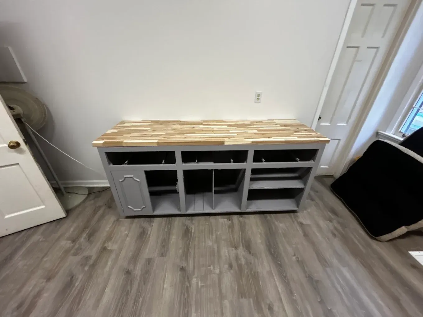 Gray cabinet with wood countertop, built-in shelves and wine rack, set against a white wall.