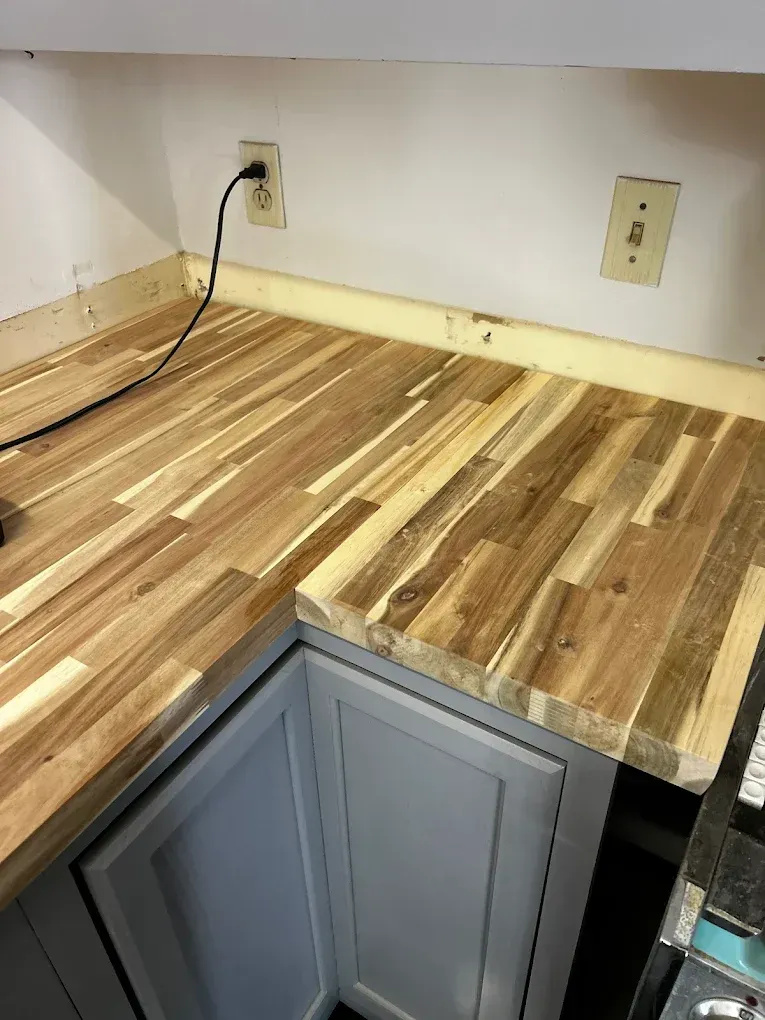 Wooden butcher block countertop over gray cabinets. Electrical outlets on the white wall.