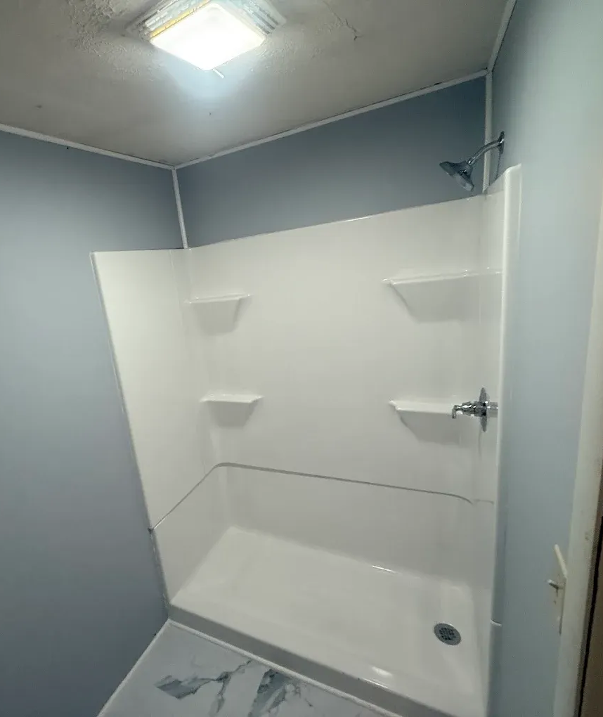 White shower stall with three shelves, blue walls, and silver shower head.