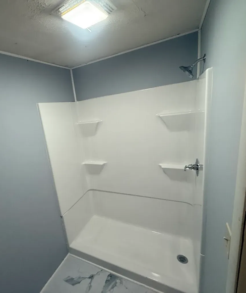 White shower stall with three built-in shelves against blue walls; chrome faucet and showerhead.