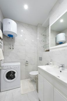 White bathroom with washing machine, water heater, toilet, sink, and mirror.