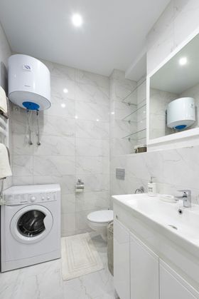 White bathroom with washing machine, water heater, toilet, sink, and mirror.