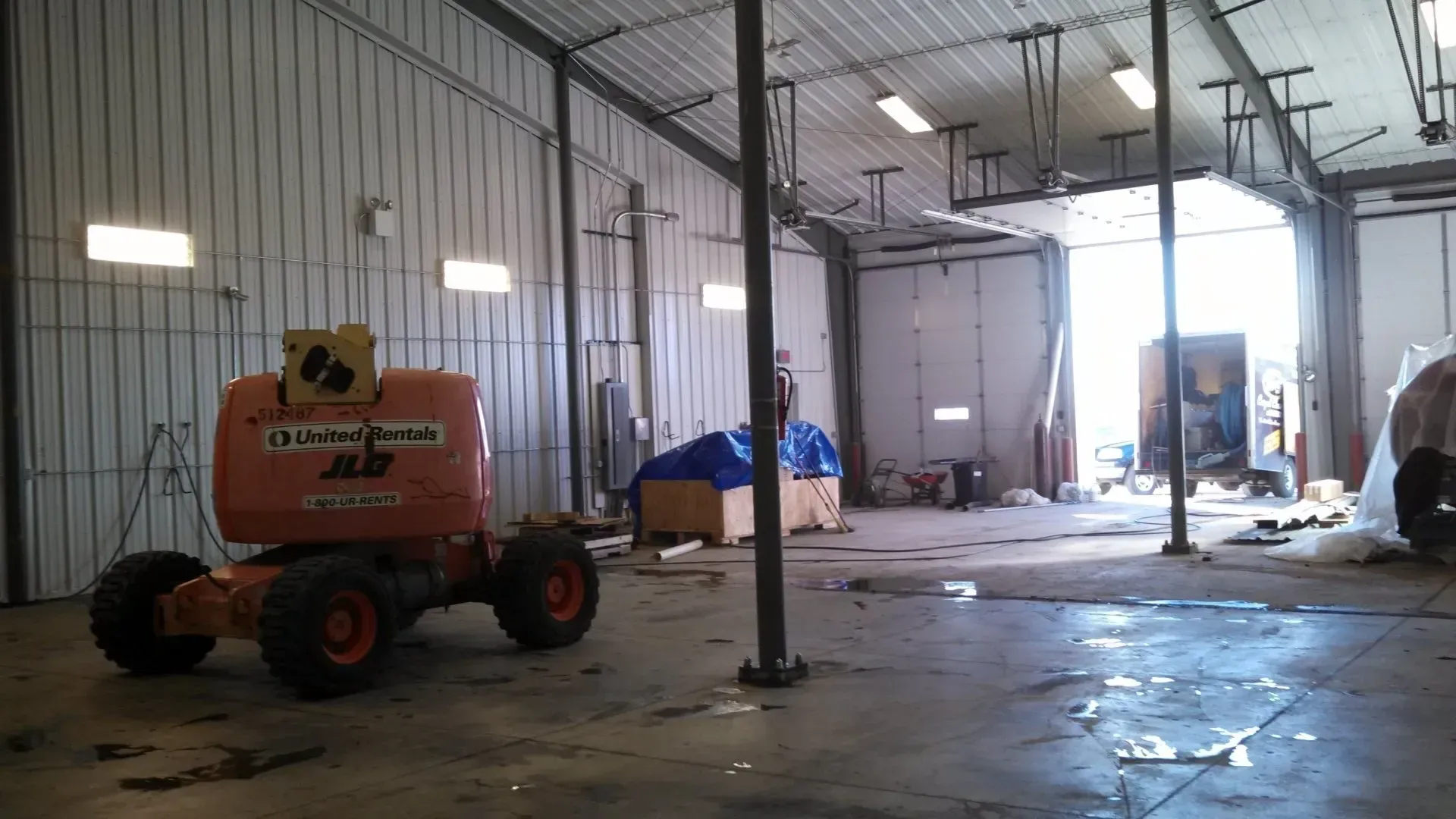 Orange aerial lift in a large, empty industrial building with a large open doorway.