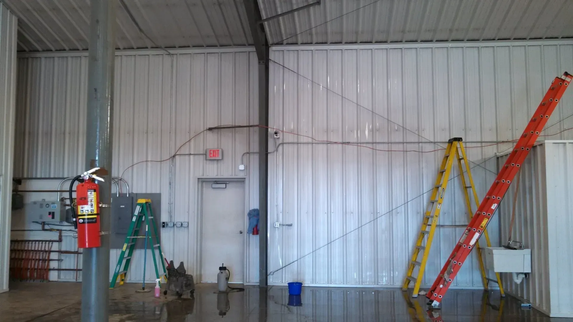 Interior of a building with water on the floor, ladders, fire extinguisher, and a door.