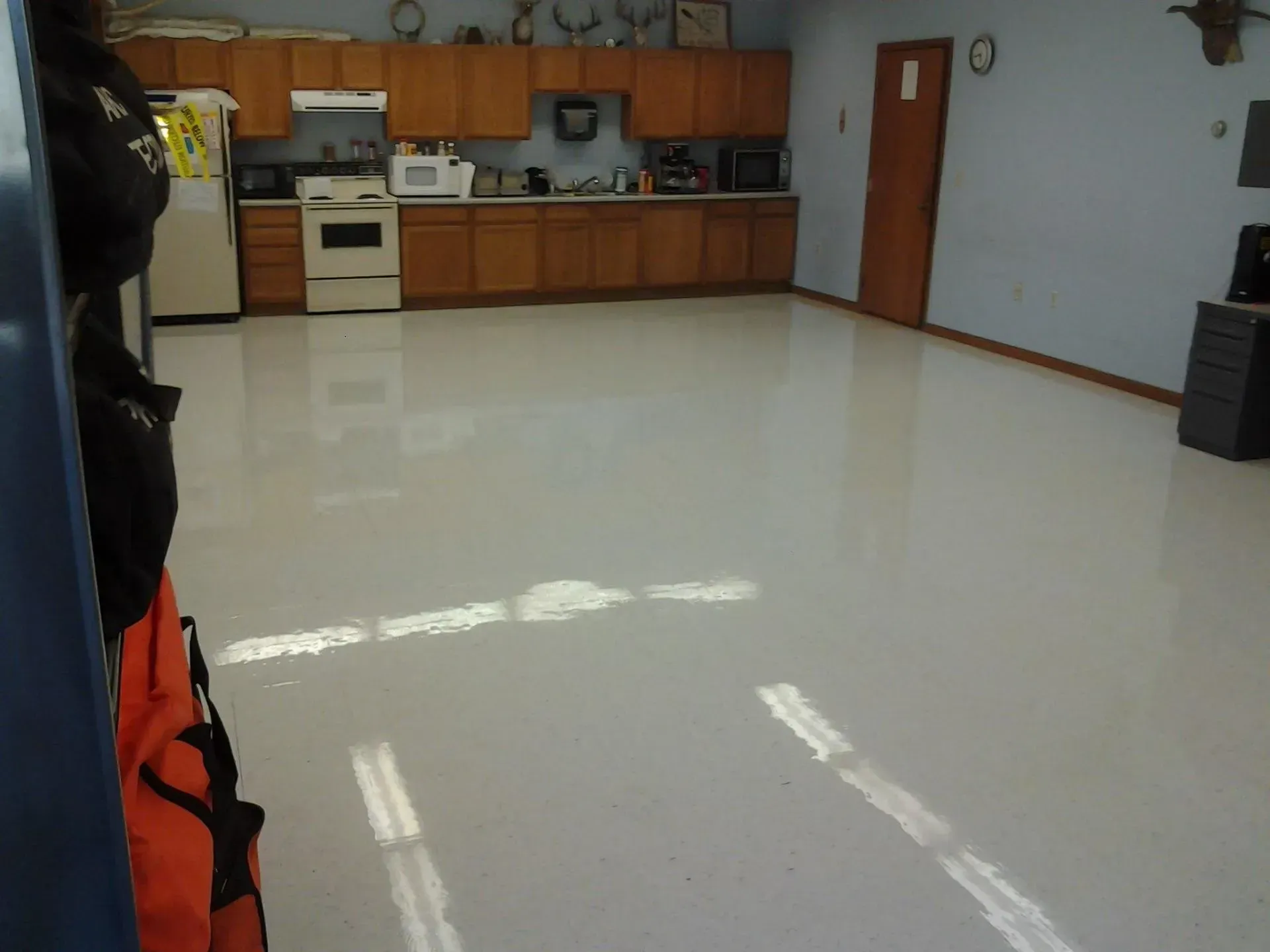 Shiny, light-colored floor in a room with a kitchen in the background, a closed wooden door, and a black bag hanging.