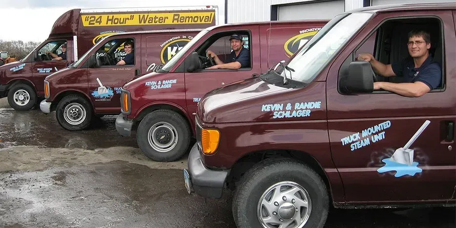 A red K&S Carpet Cleaners truck with a man and woman shaking hands in front of a house.