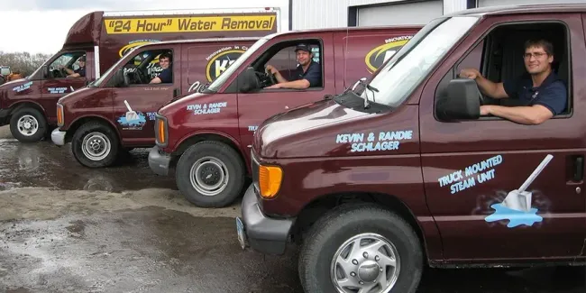 A red K&S Carpet Cleaners truck with a man and woman shaking hands in front of a house.