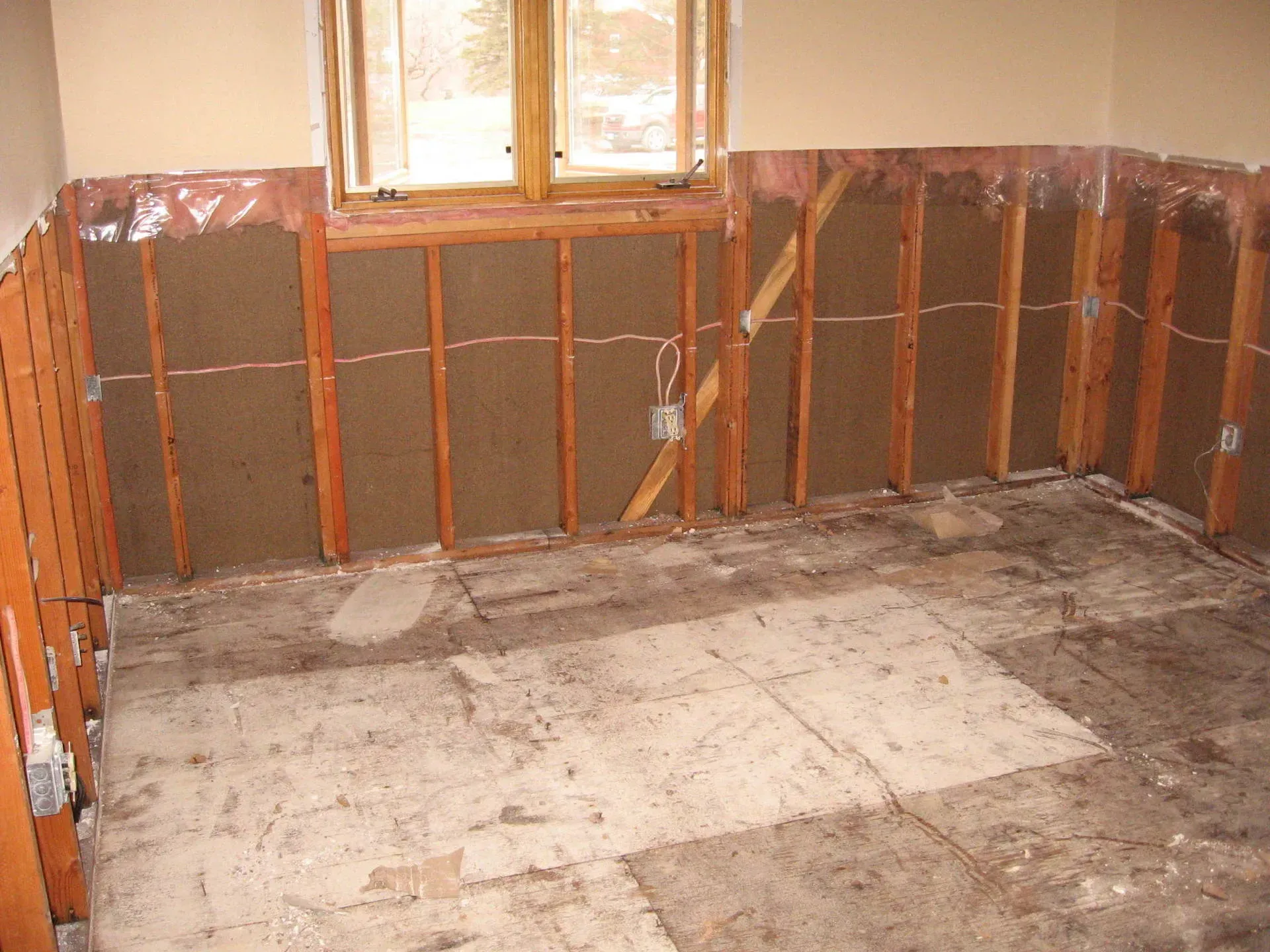 Room gutted during renovation, exposed framing, insulation, and damaged flooring.