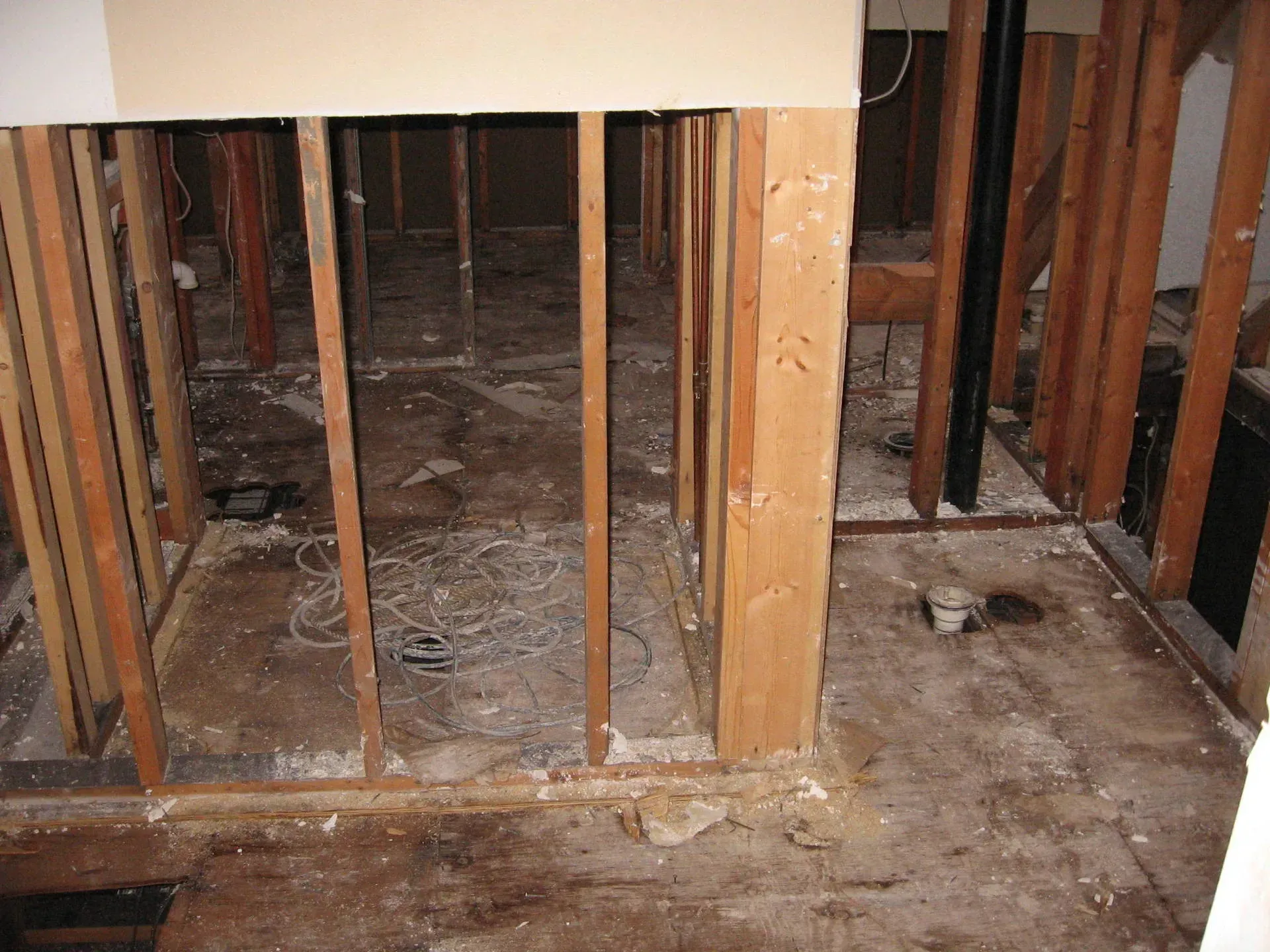 Interior view of a room gutted to the studs. Exposed wooden beams and flooring are visible.