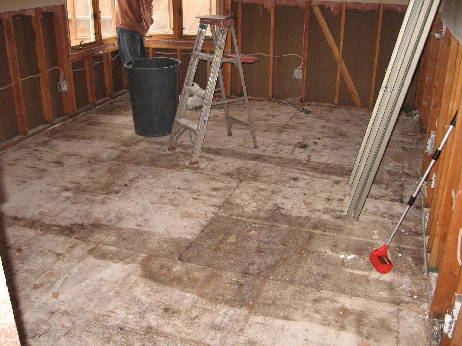 Room under renovation: exposed walls and floor, ladder, bucket, person, and tools.