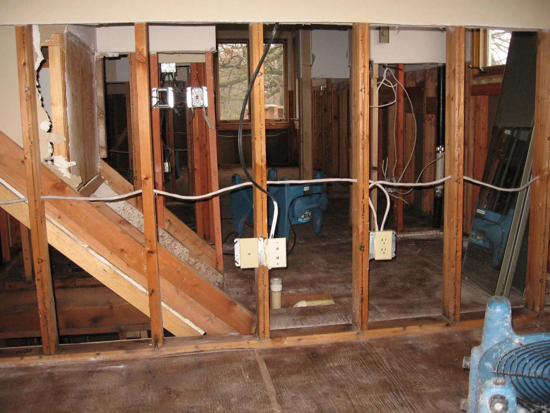 Interior wall demolition showing exposed studs, electrical wiring, and outlets; water damage present.