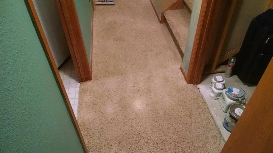 Beige carpeted hallway with doorways, stairs, and paint supplies.