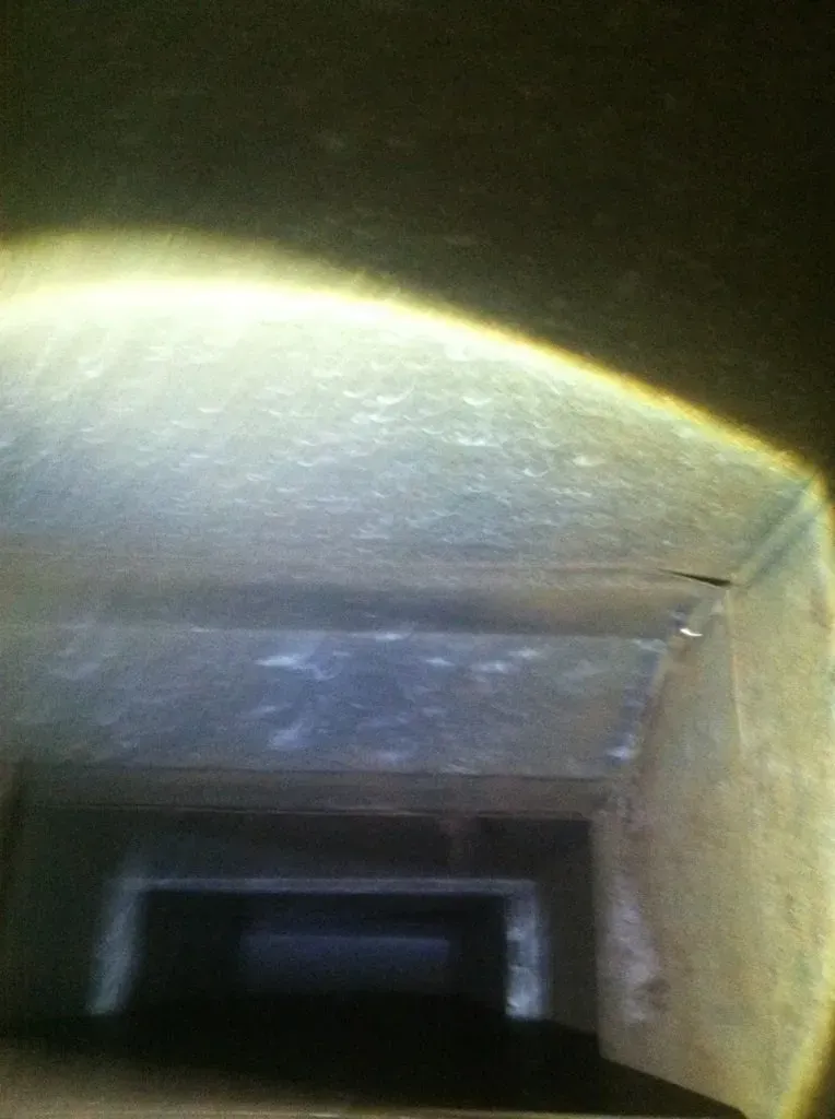 Looking down a rectangular, dusty duct, lit with a bright flashlight.