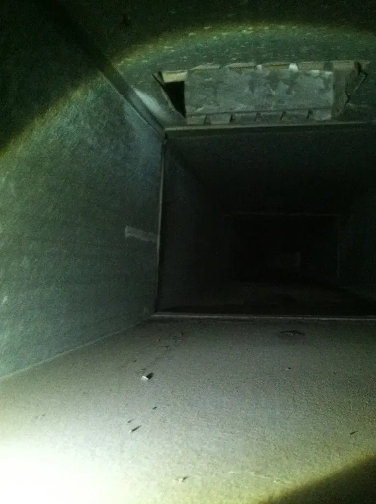 Inside view of a rectangular air duct, dark interior with a visible opening and metal walls.