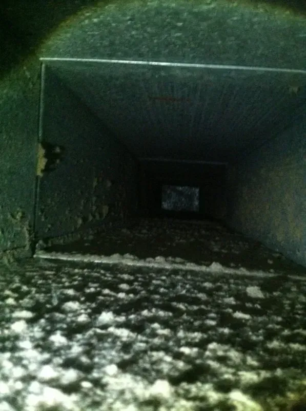 Inside of a dirty air duct, covered with dust and debris. Dark interior.