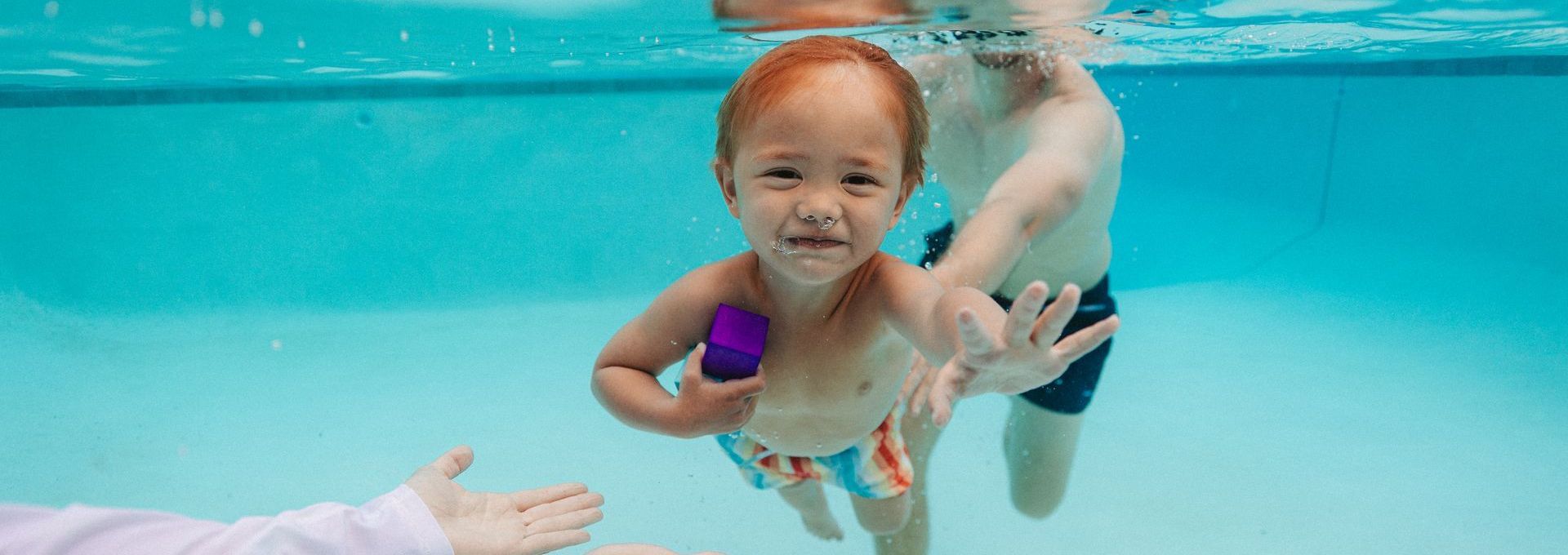 A boy and a girl are swimming underwater in a pool.