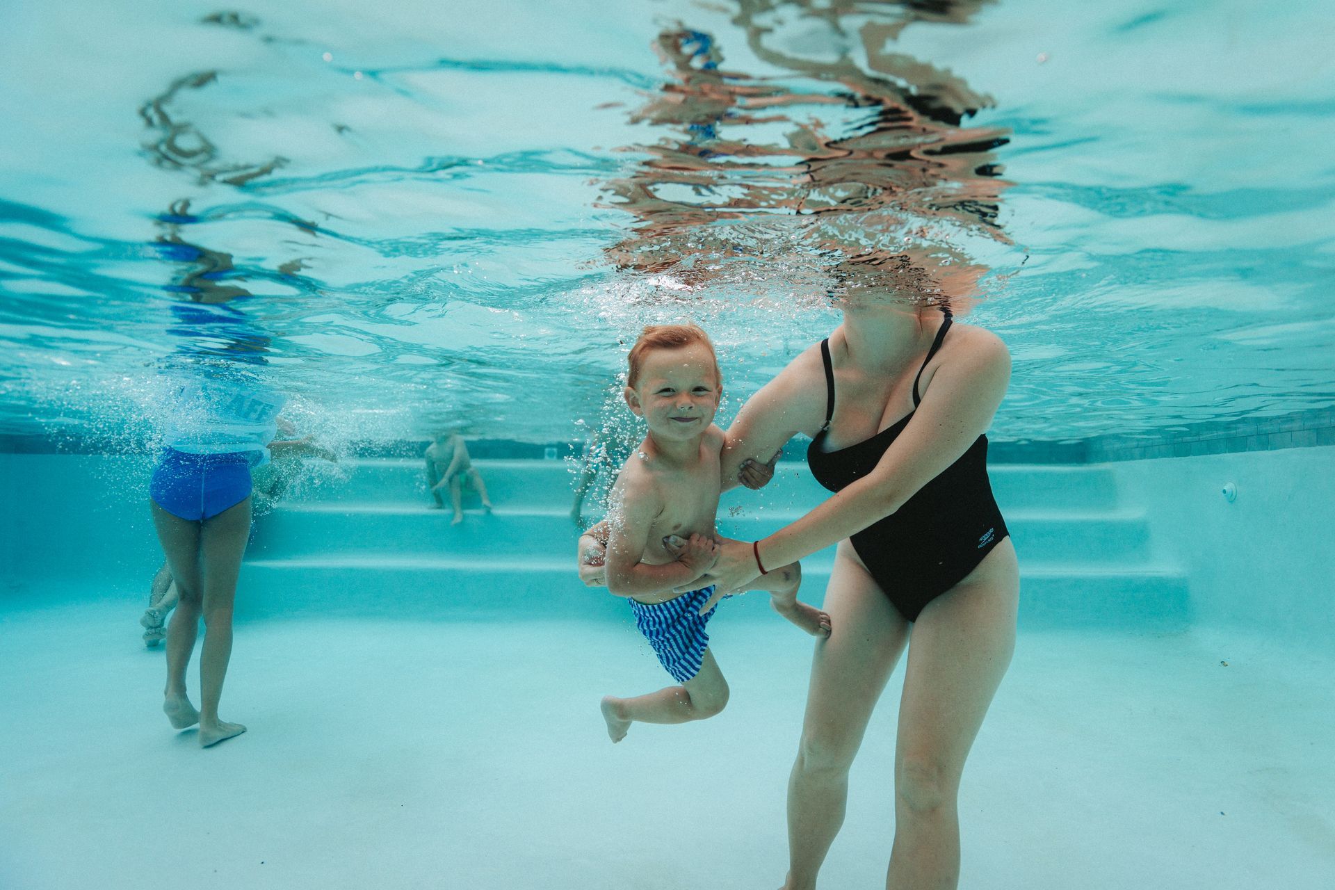 A woman is holding a child underwater in a swimming pool.