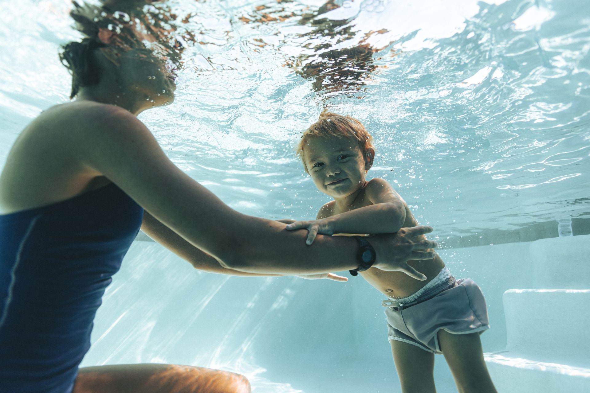 A woman and a child are swimming underwater in a pool.