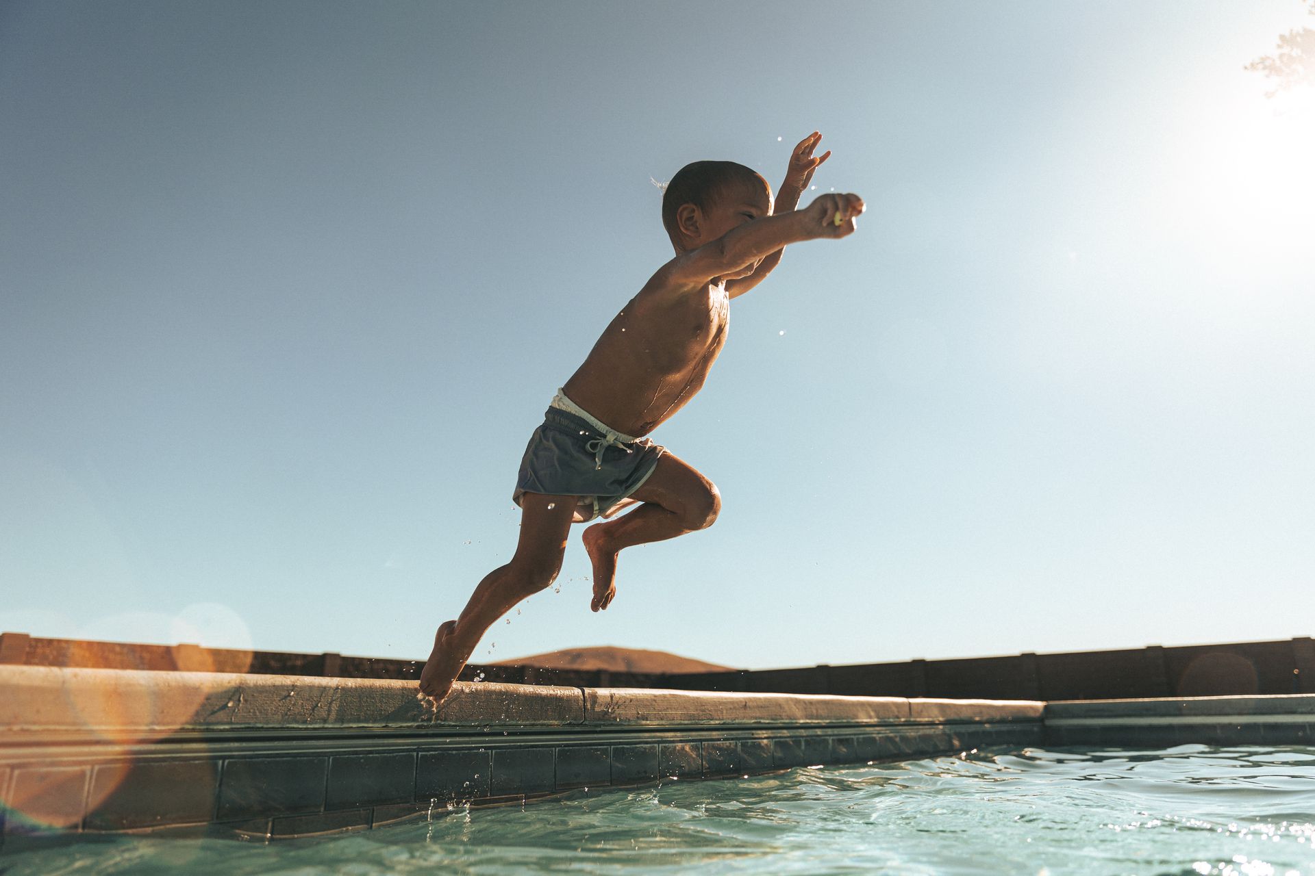 A young boy is jumping into a swimming pool.