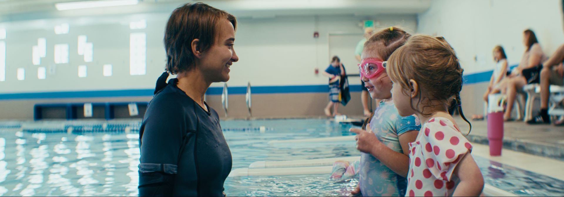 A woman is talking to two little girls in a swimming pool.