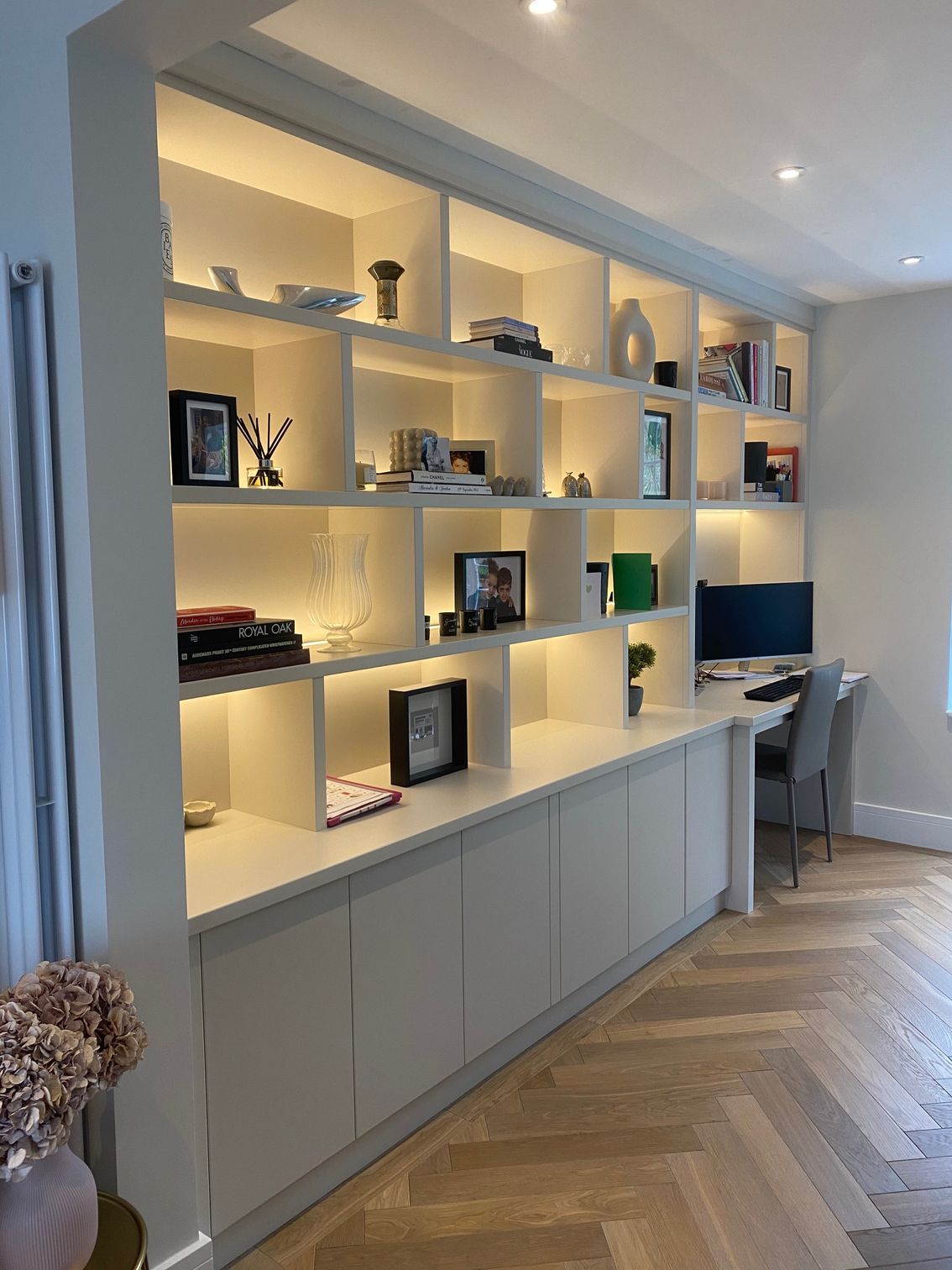 Built-in white shelves with lighting over a desk, showcasing decor and books in a bright room with wood floors.