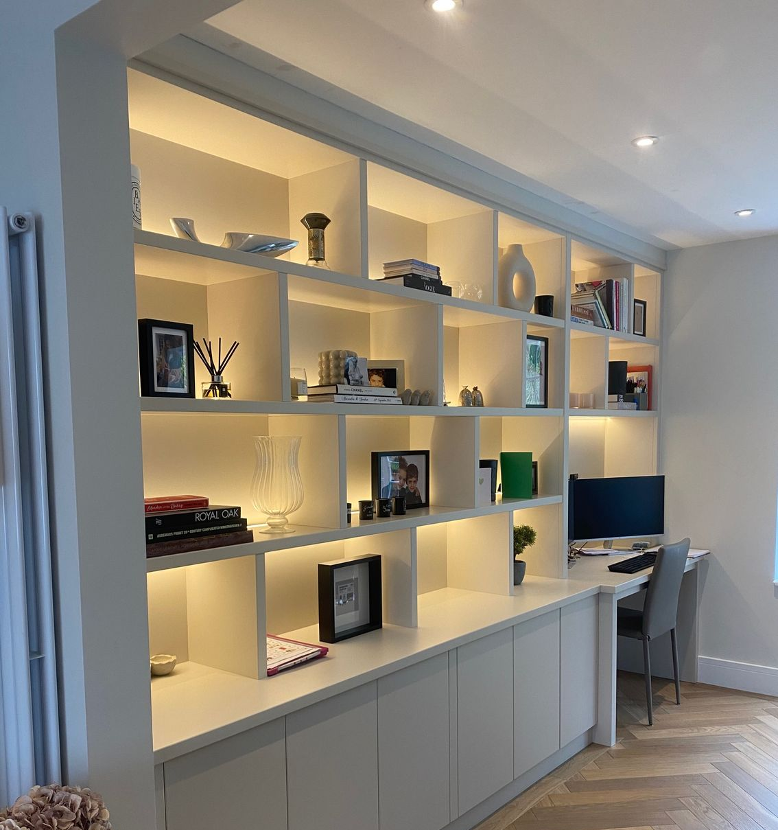 Built-in white shelving unit with interior lighting, holding various decor items and a desk with a computer.