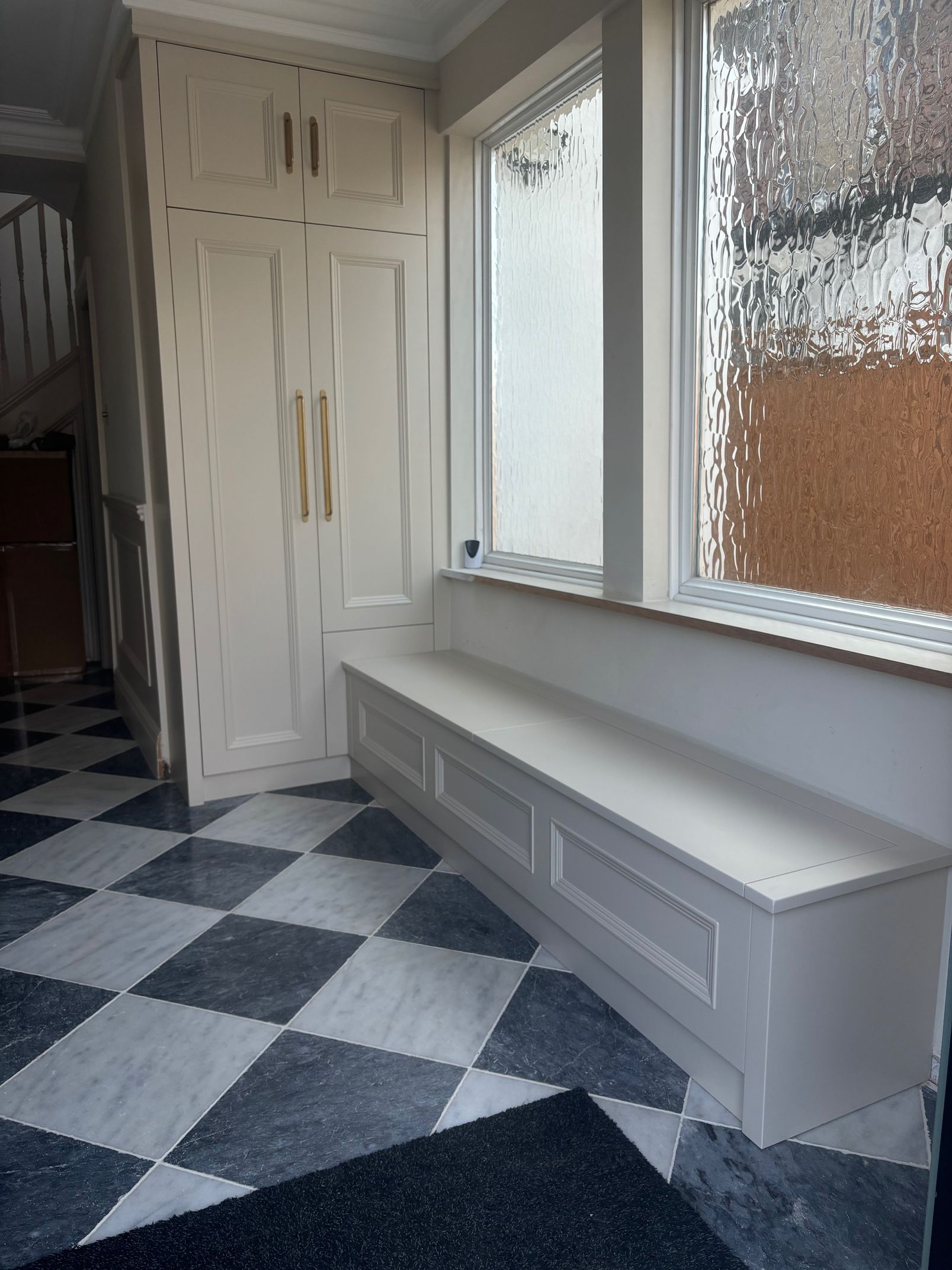 Hallway with checkered floor, built-in bench under windows, and tall white storage cabinet.