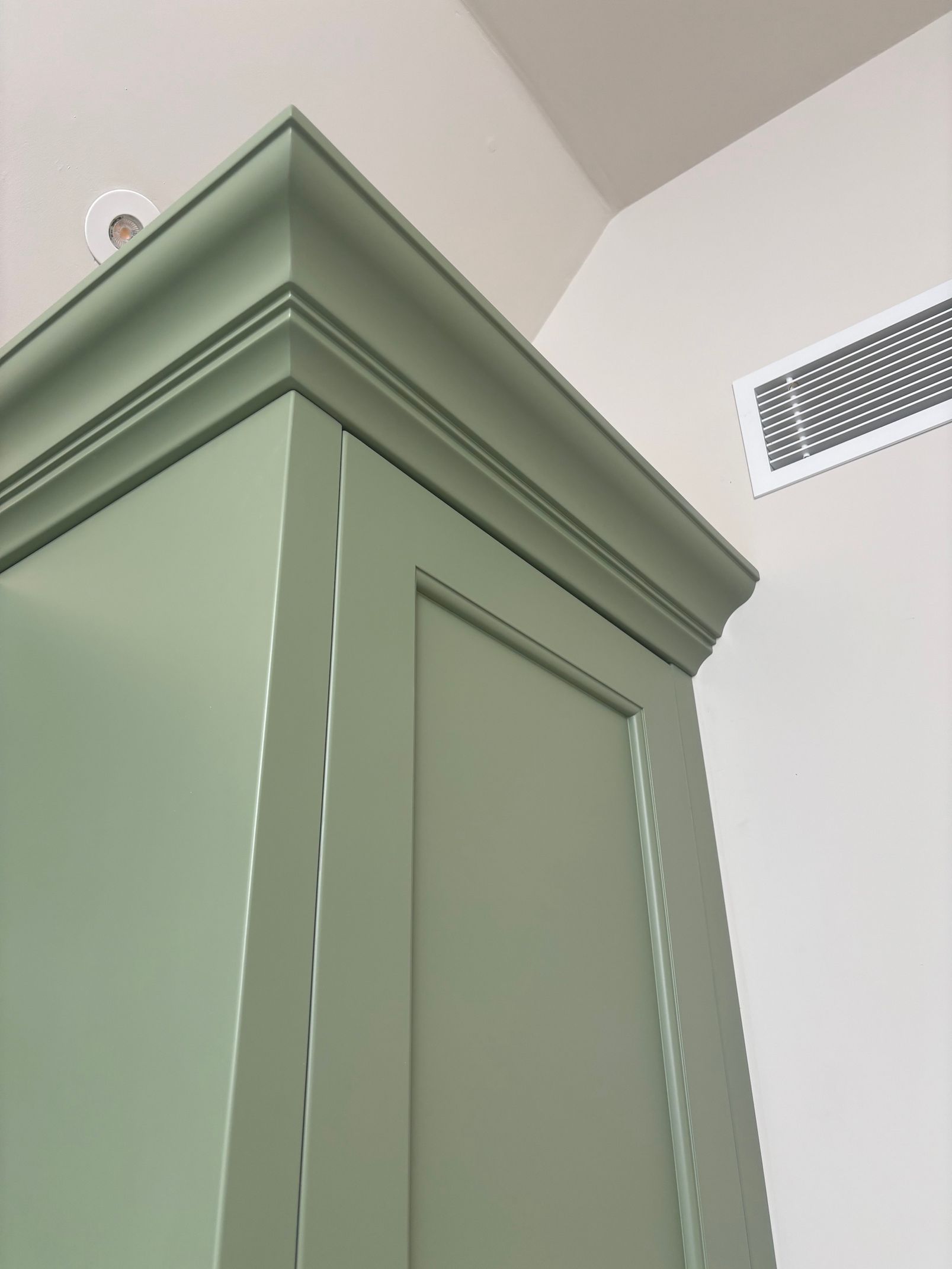 Green cabinet with detailed crown molding, corner of a room.