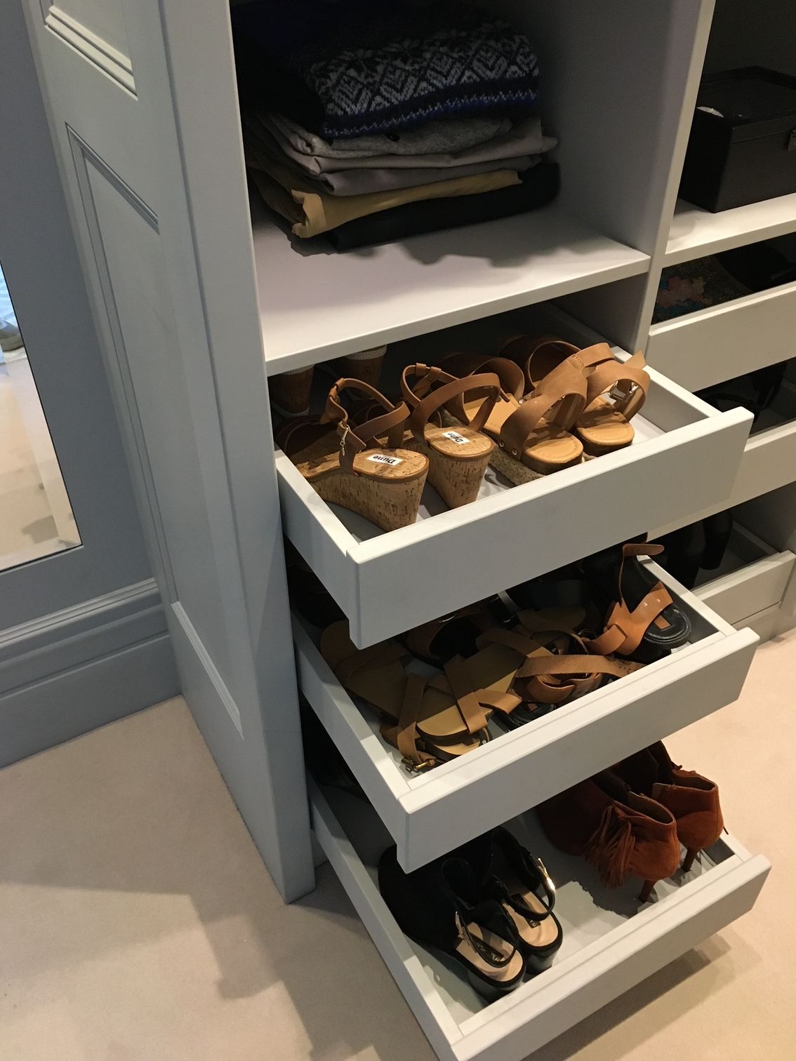 Closet with pull-out drawers filled with shoes, above folded clothes. Light blue cabinetry with white shelves.