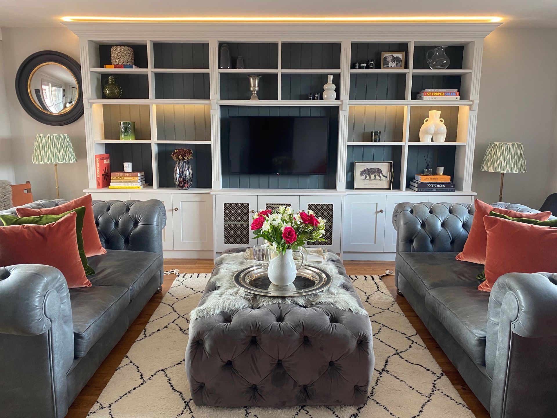 Living room with gray sofas, built-in shelving, TV, and tufted ottoman.