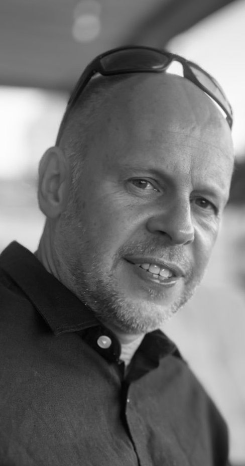 Man with short hair and sunglasses on his head smiling. Black and white photo.