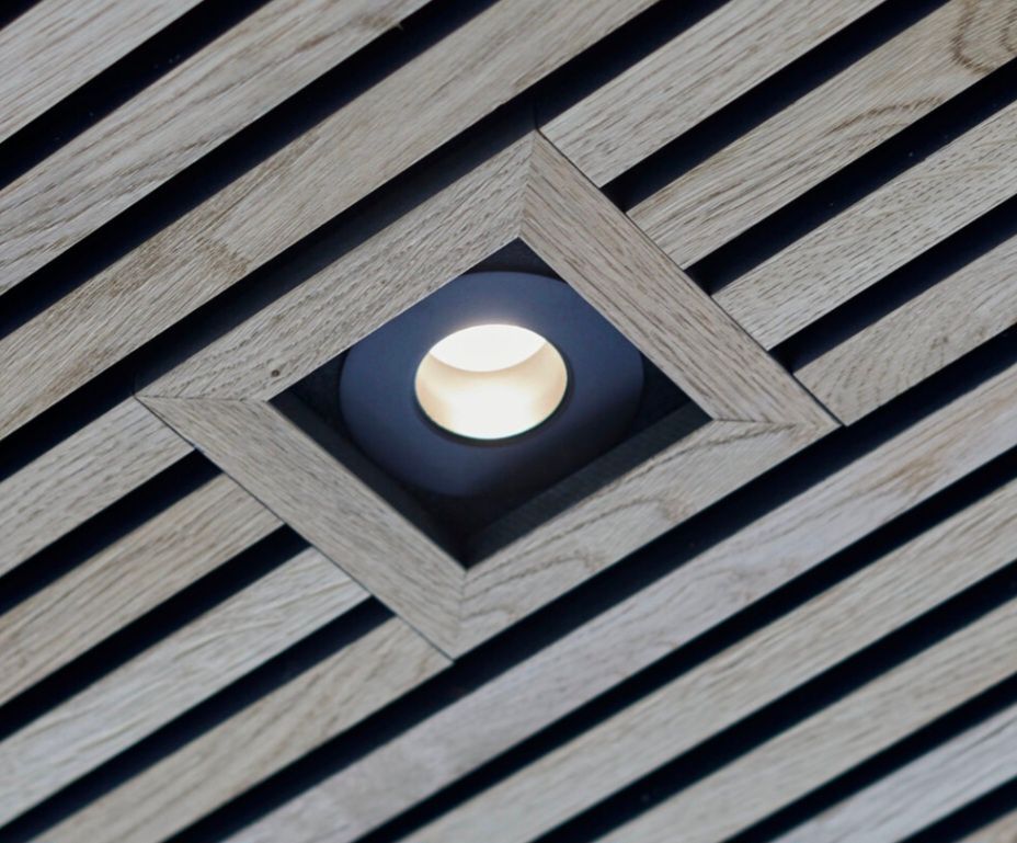 Close-up of a recessed ceiling light surrounded by diamond-shaped wood paneling on a slatted wood ceiling.