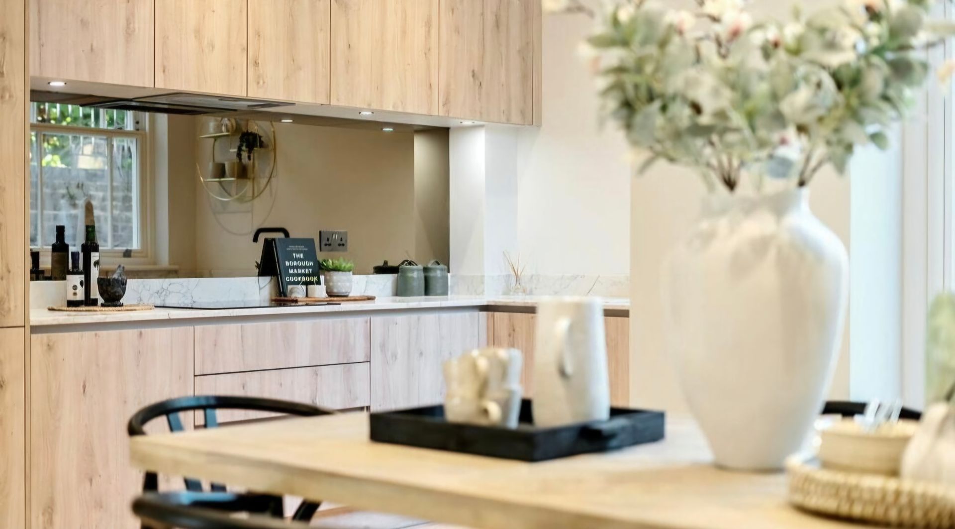 Kitchen interior with wooden cabinets, a dining table with a vase of flowers, and kitchen counter in the background.
