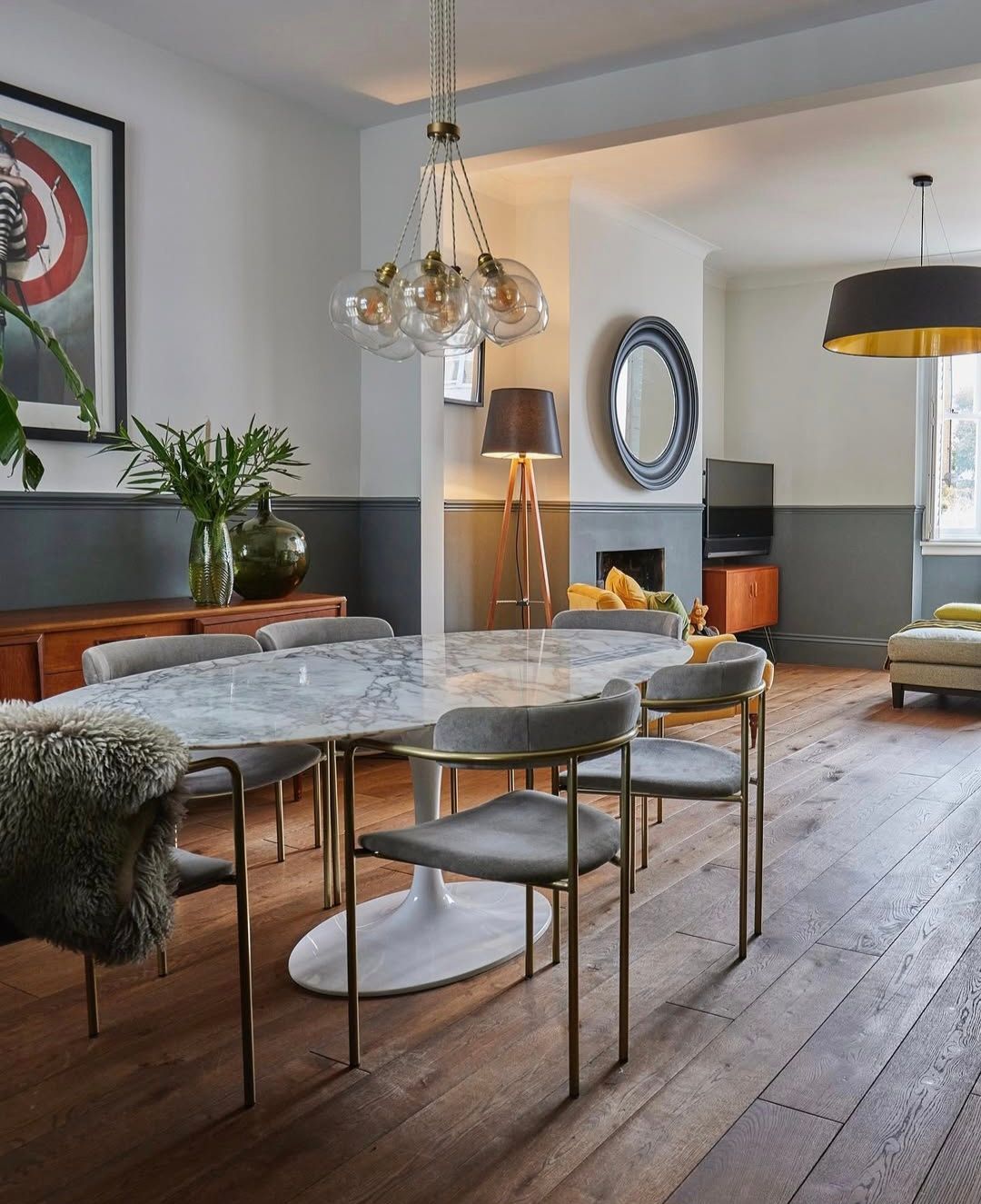 Dining room with oval marble table, gray chairs, and hanging light fixture.