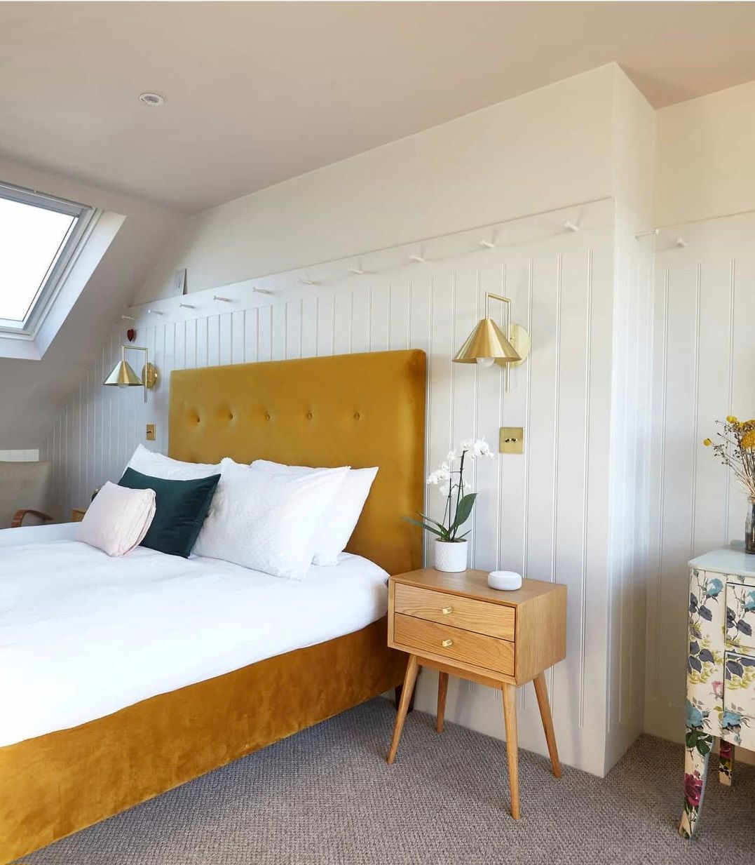 Bedroom with a mustard yellow bed, wooden nightstand, and floral patterned drawer.