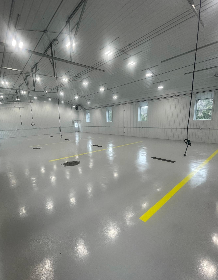 Brightly lit, empty warehouse with gray floor, white walls, and yellow markings.