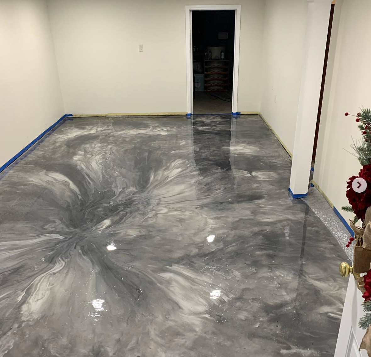 Metallic gray and white epoxy floor in a room, reflecting light. Doorway in the back and a partial Christmas decoration.