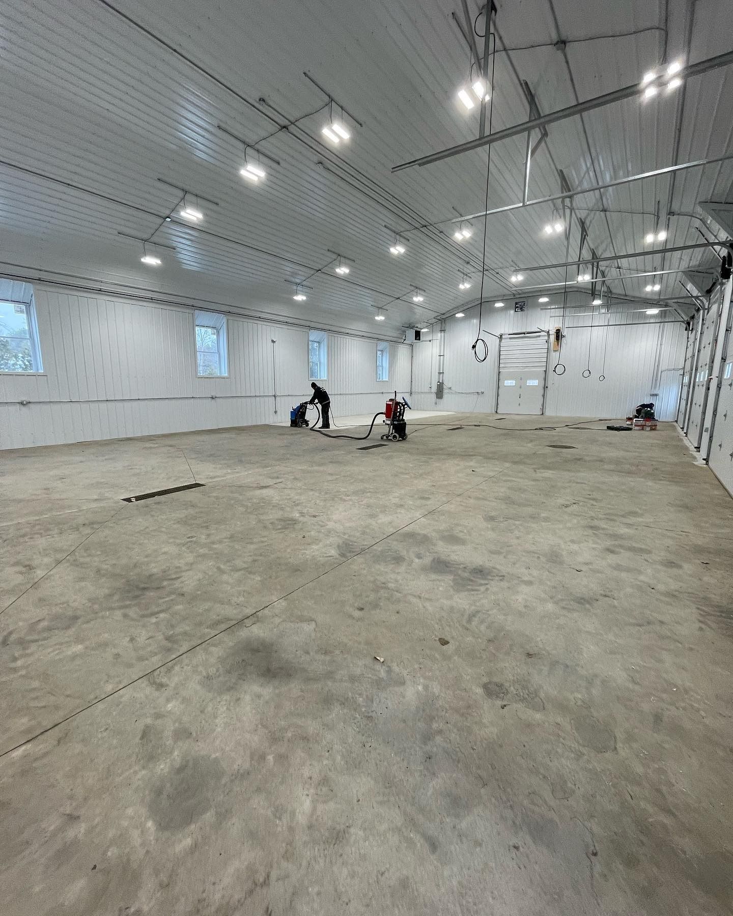 Workers inside a large, empty warehouse with concrete floor, overhead lights, and white walls.